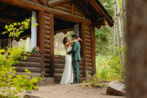 Couple shares first dance outside rustic log cabin wedding venue surrounded by lush forest trees.