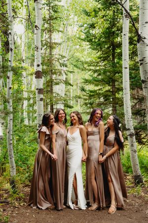 Bride and four bridesmaids in taupe gowns pose together in an aspen forest during a summer wedding.