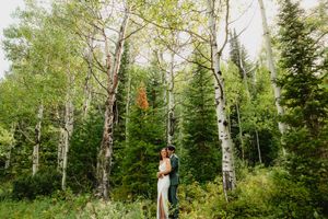 Bride and groom embracing in a lush forest of aspen and pine trees during an outdoor wedding ceremony.