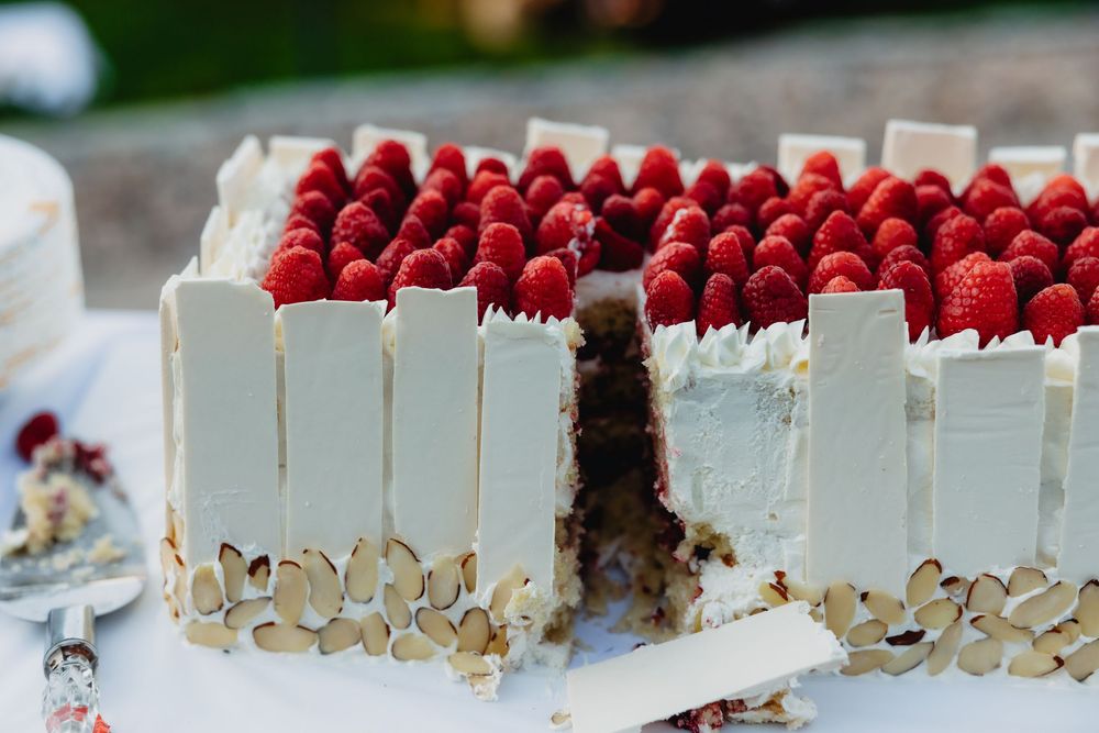 Elegant rectangular white chocolate cake topped with fresh raspberries and almond slices on a white table.