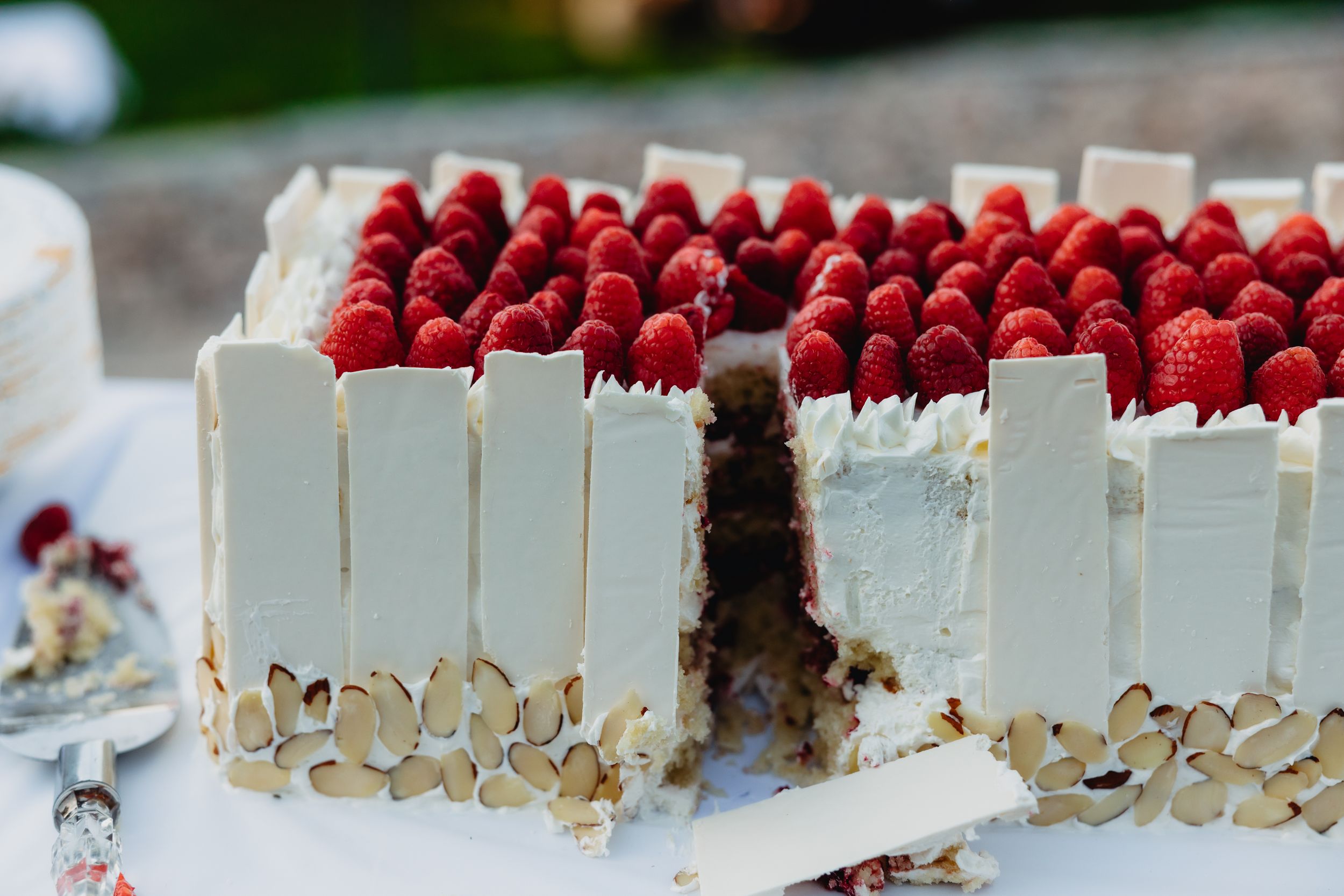 Elegant rectangular white chocolate cake topped with fresh raspberries and almond slices on a white table.