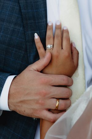 Close-up of newlywed couple hands showing diamond engagement ring and gold wedding band.