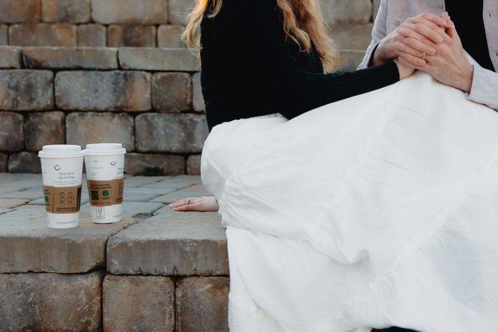 Bride and groom sitting together on stone steps with two coffee cups beside them on their wedding day.