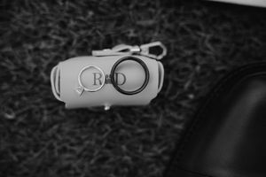 Black and white photo of wedding rings resting on a monogrammed leather key fob on grass.