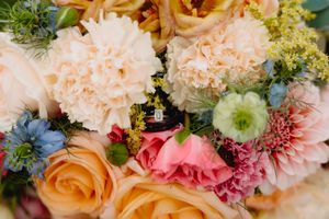Close-up of a vibrant wedding bouquet featuring peach roses, white carnations, pink flowers, and blue accents.