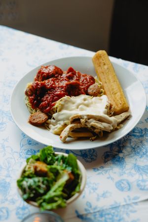 Italian dinner plate with spaghetti, meatballs in marinara, cheesy chicken, garlic bread, and fresh green salad.