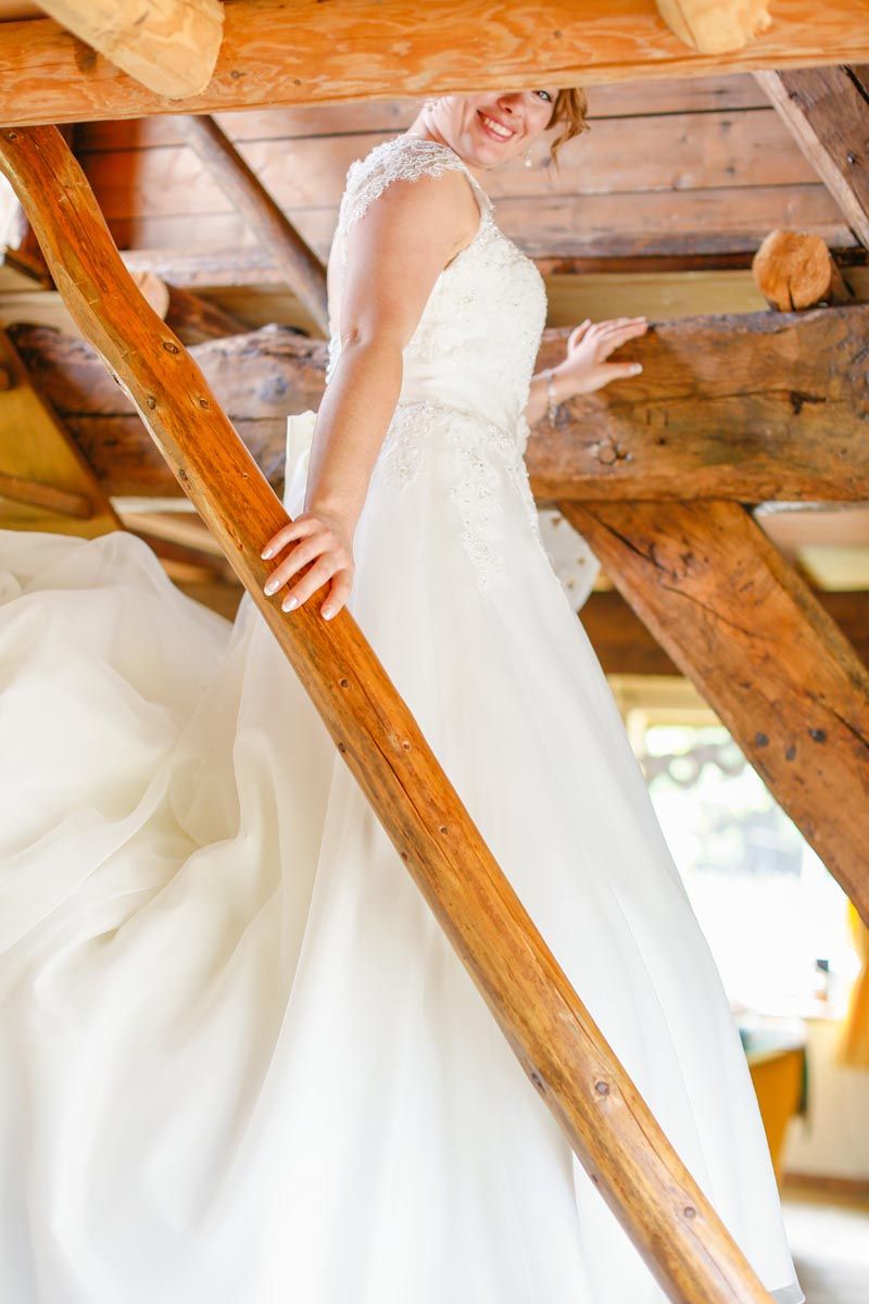 Close-up detail of white lace wedding dress against rustic wooden beams.