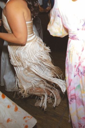Woman wearing a white fringed dress dancing at a party next to a guest in a floral maxi dress.