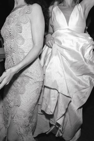 Black and white photo of two women in elegant gowns, one lace dress and one satin wedding dress.