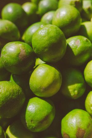 A pile of fresh green limes with textured skin, closely packed together in natural lighting.