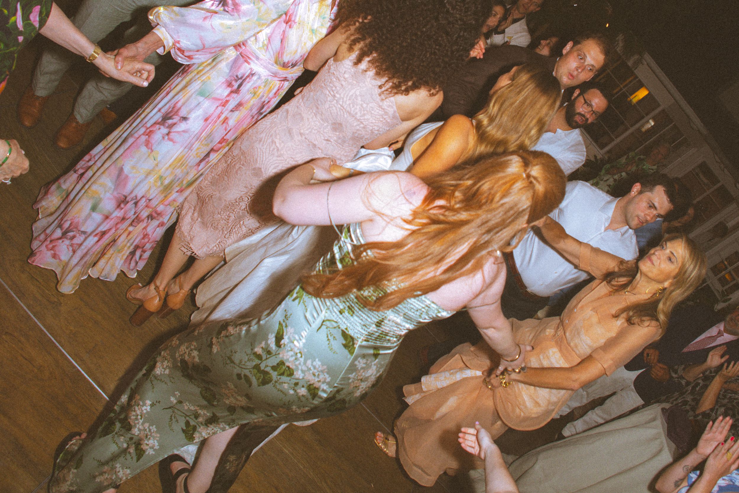 Group of guests dancing and socializing at an indoor party event on a wooden dance floor.