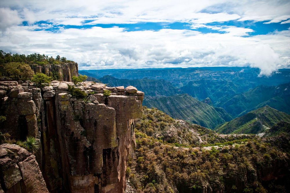 Piedra Volada, La Sierra Tarahumara, ChihuahuaRocky cliffs and steep canyon walls overlooking a vast mountain valley under blue skies.