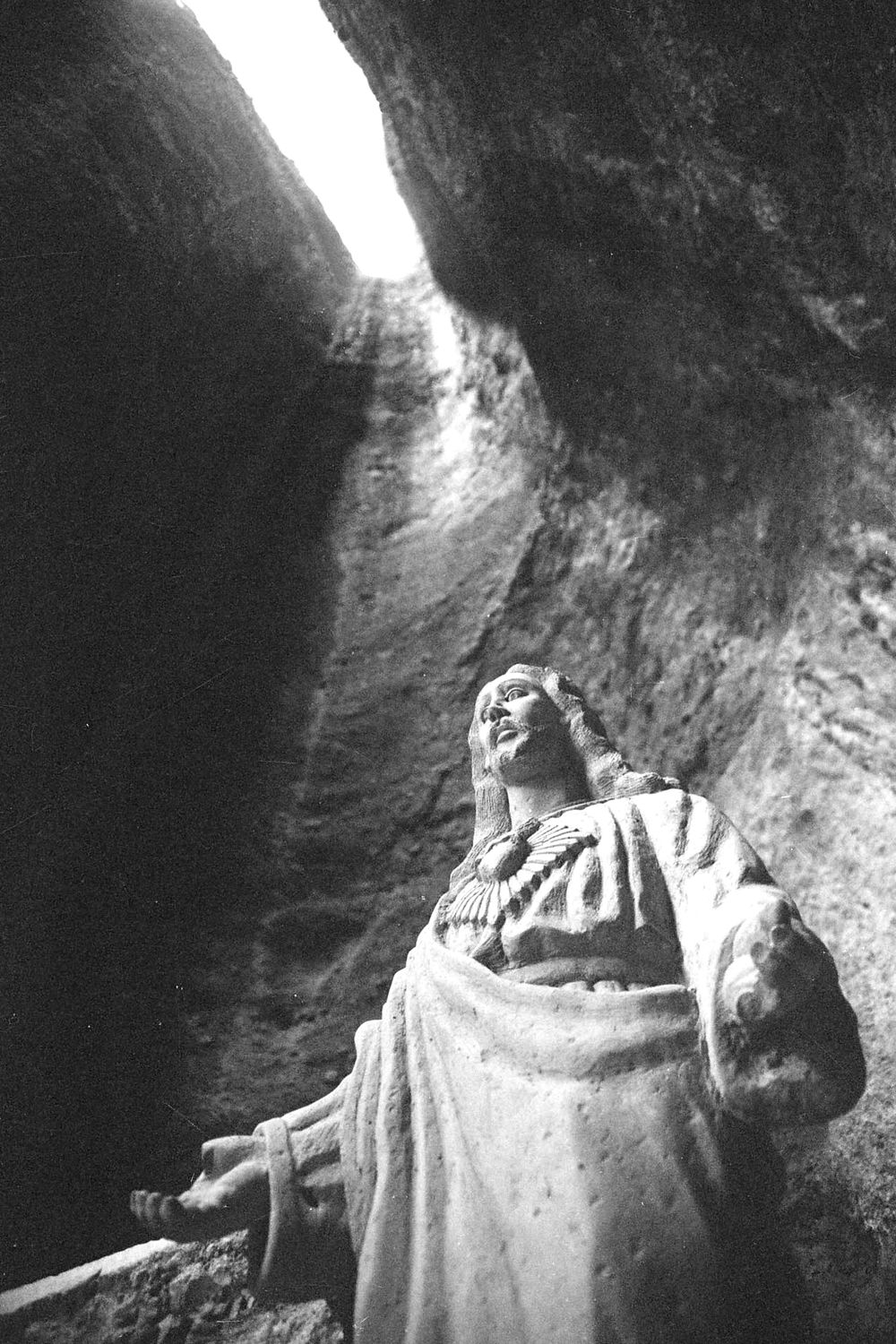 Black and white image of a religious statue photographed from below against rocky walls.