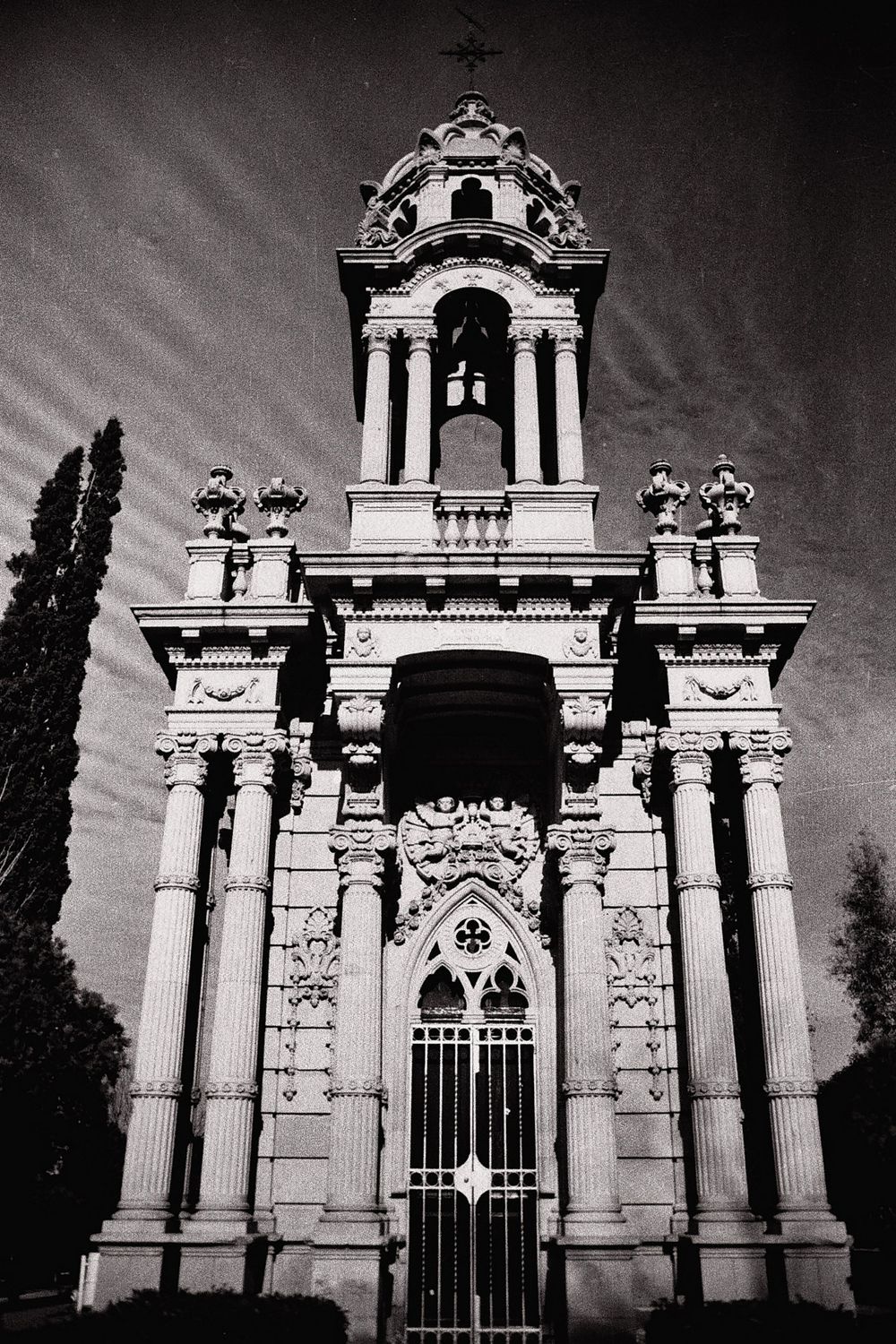 Gothic-style bell tower and ornate gate photographed in dramatic black and white.