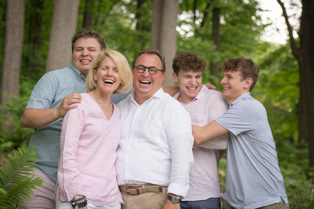 A joyful family of five laughing together outdoors in a lush green forest setting.