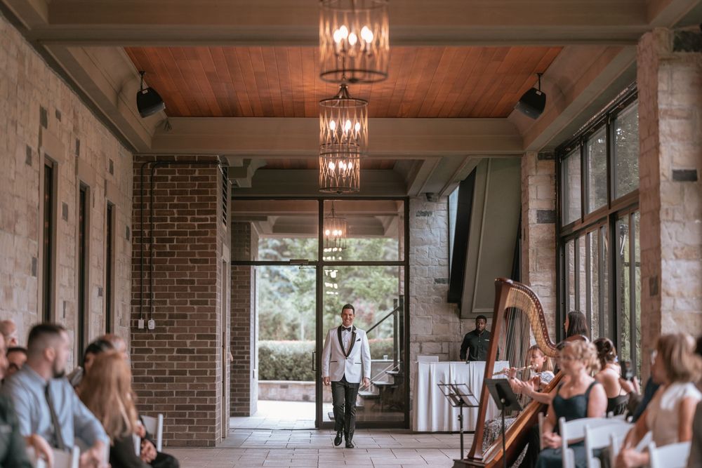 Elegant wedding ceremony in a brick venue with chandeliers, a harpist, and a groom walking down the aisle.