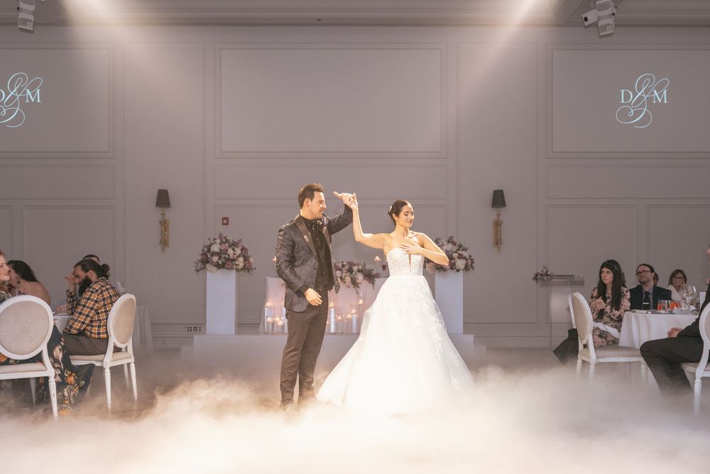 Bride and groom share first dance on fog-covered floor in elegant wedding ballroom with monogram backdrop.