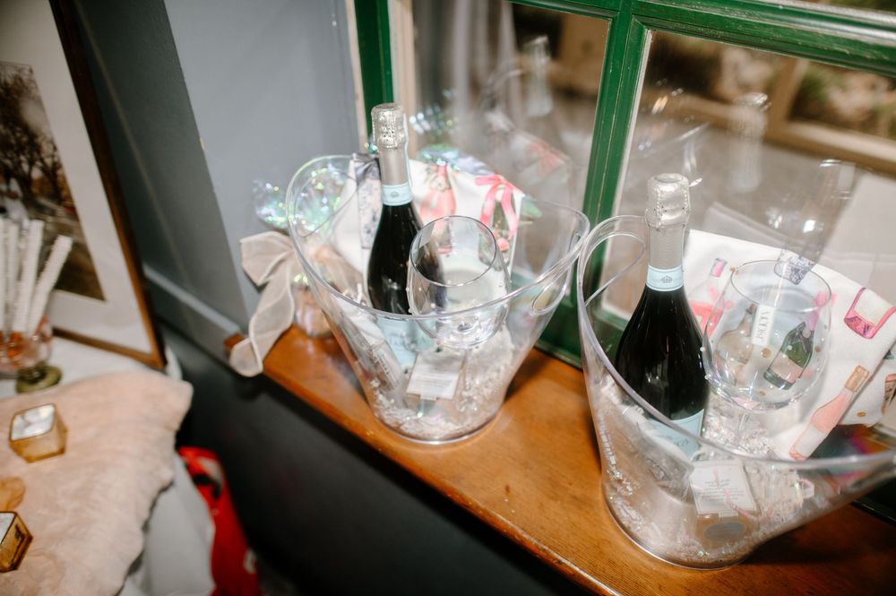 Clear ice buckets with champagne bottles and decorative bows displayed on a wooden shelf near a window.