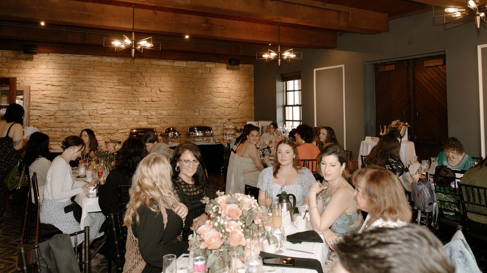 Guests gathered at elegantly set tables in a rustic brick-walled banquet hall during a wedding reception event.