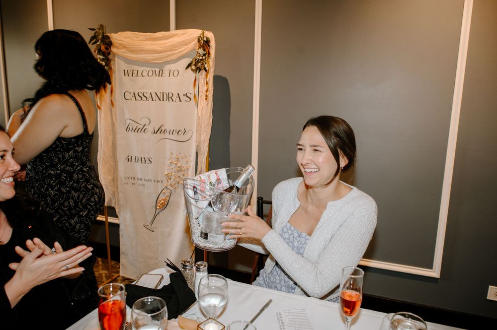 Woman smiling at bridal shower holding gift bag next to welcome banner at elegant party.