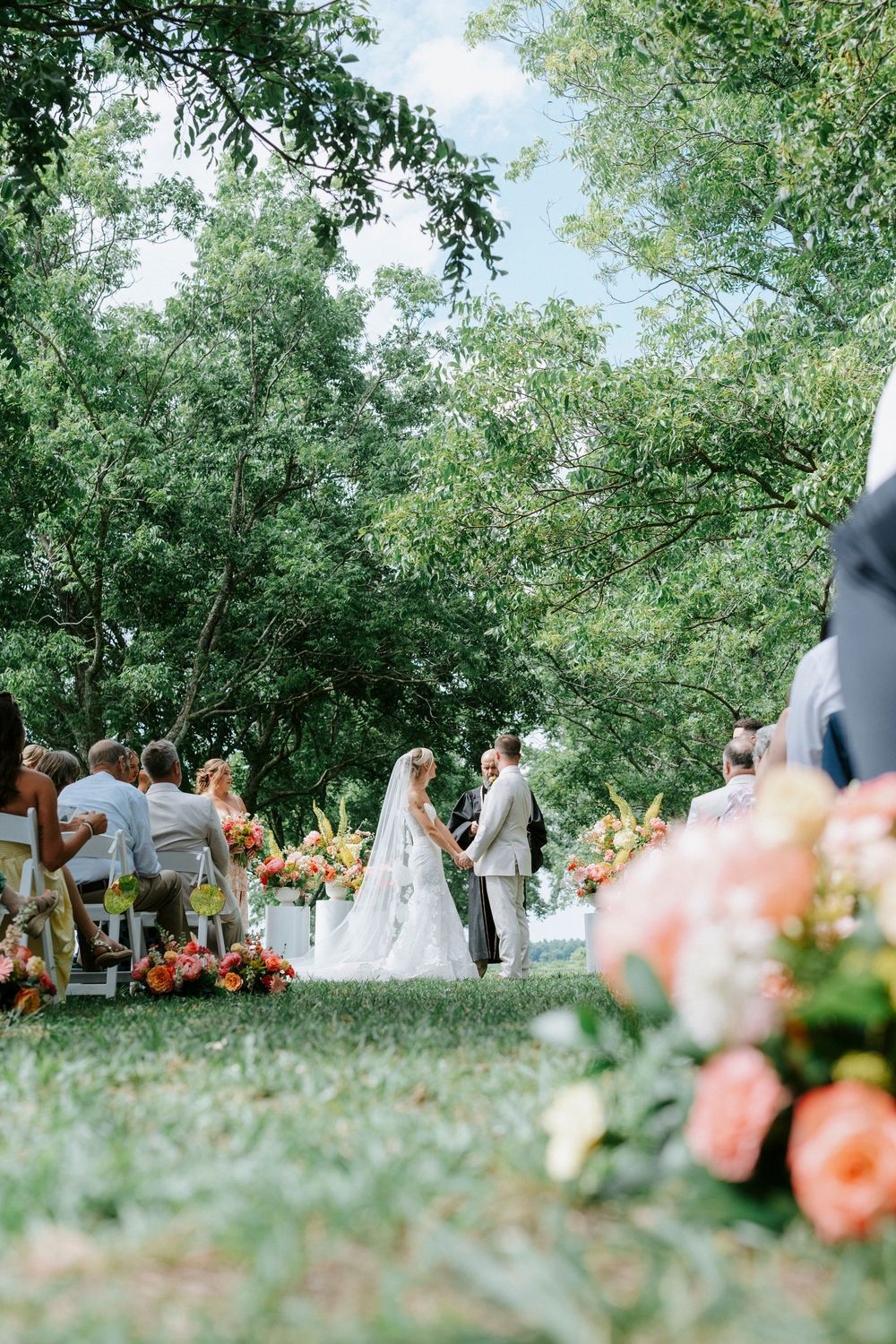 Outdoor garden wedding ceremony with bride and groom at altar surrounded by colorful florals.