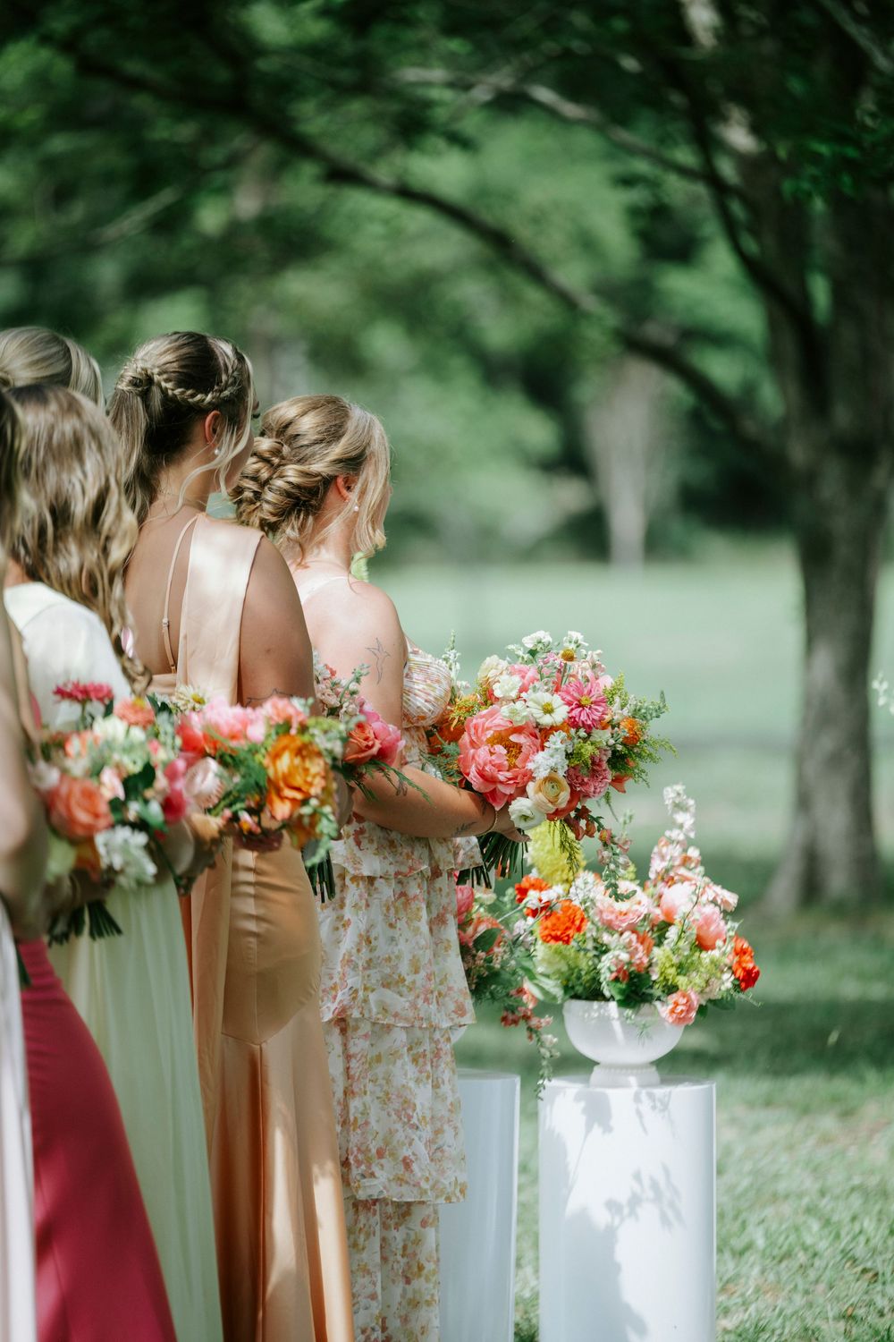 Bridesmaids in champagne and floral dresses hold vibrant pink and orange bouquets outdoors.