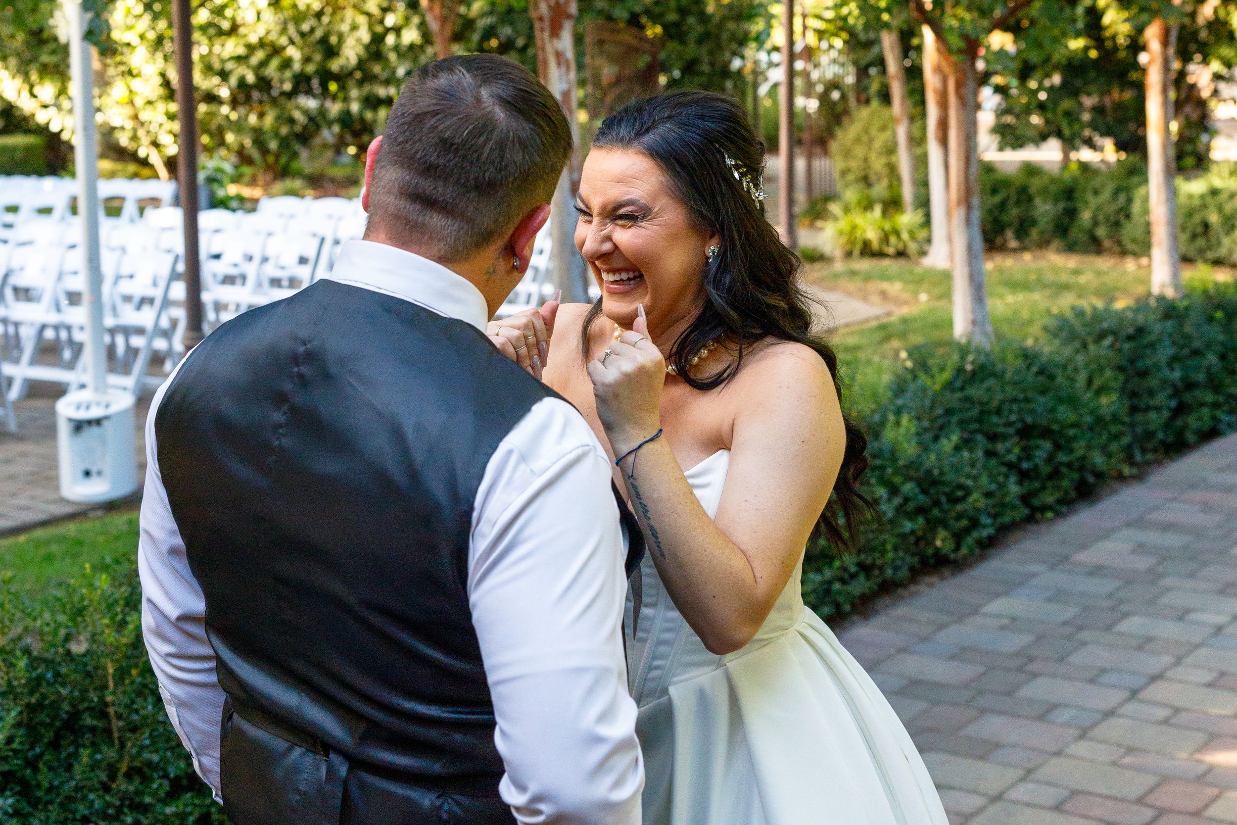 Bride laughing joyfully with groom during outdoor wedding first look in a garden setting.