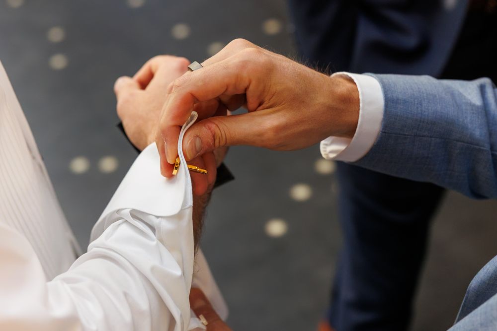Close-up of a man fastening a gold cufflink on a white dress shirt sleeve at a formal wedding event.