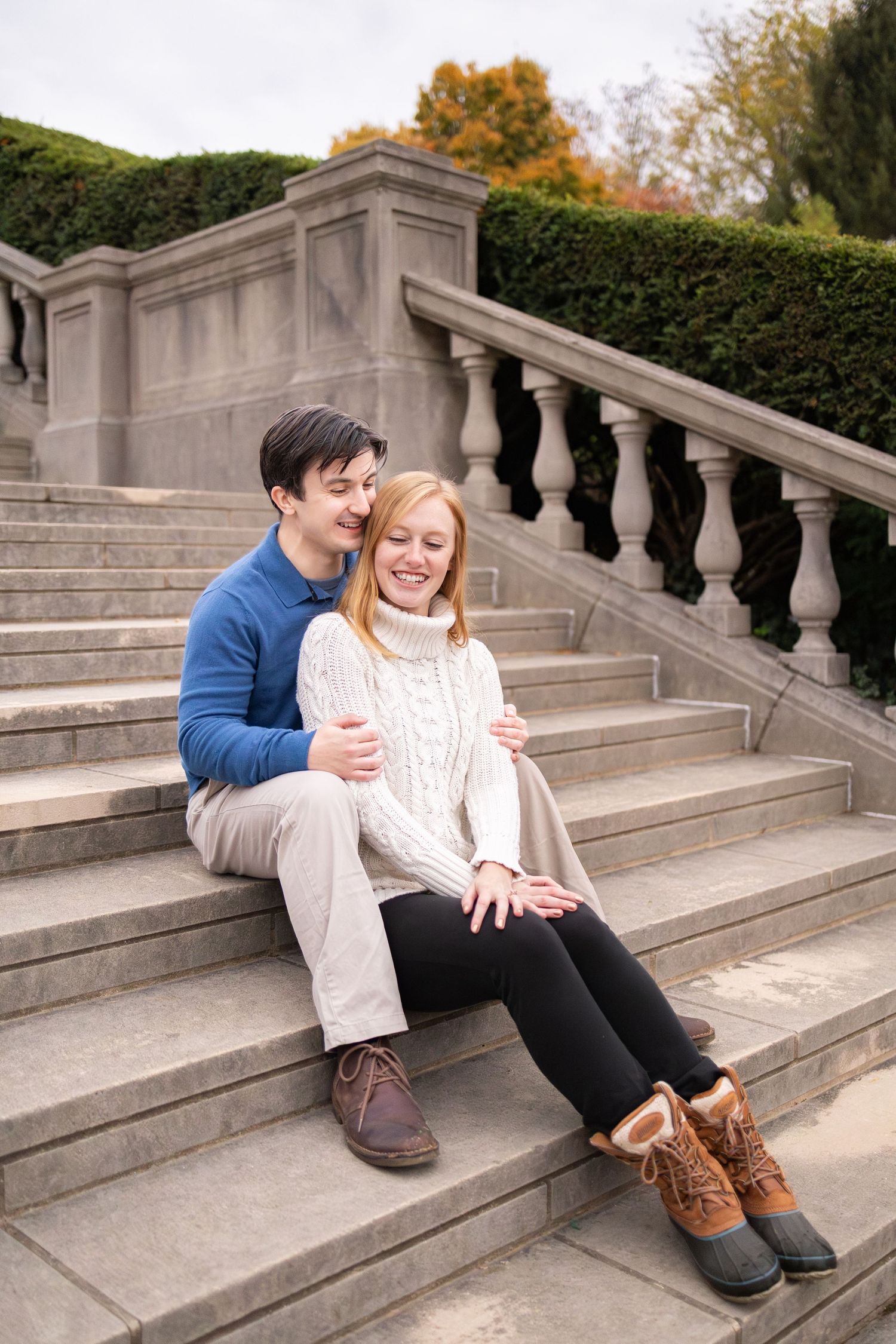 Couple sitting on stone steps outdoors at Ault Park in Cincinnati during their fall engagement photoshoot.