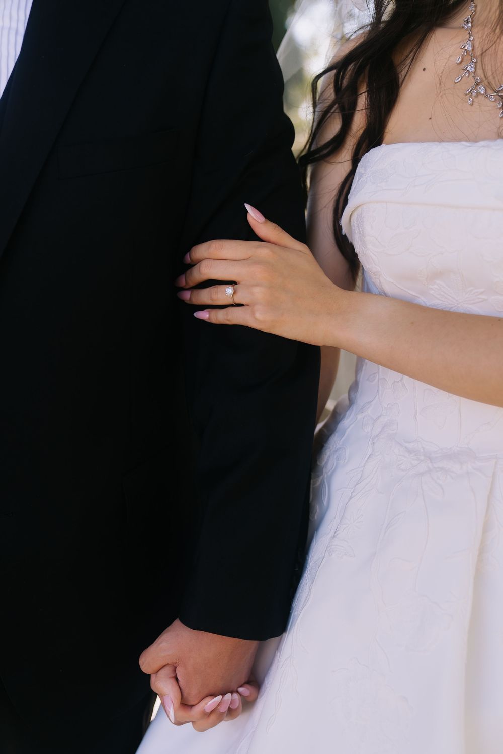 Bride in white strapless gown holding grooms arm showing diamond engagement ring while holding hands.
