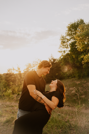 A couple shares a joyful embrace at golden hour, laughing together outdoors with warm sunlight glowing behind them.