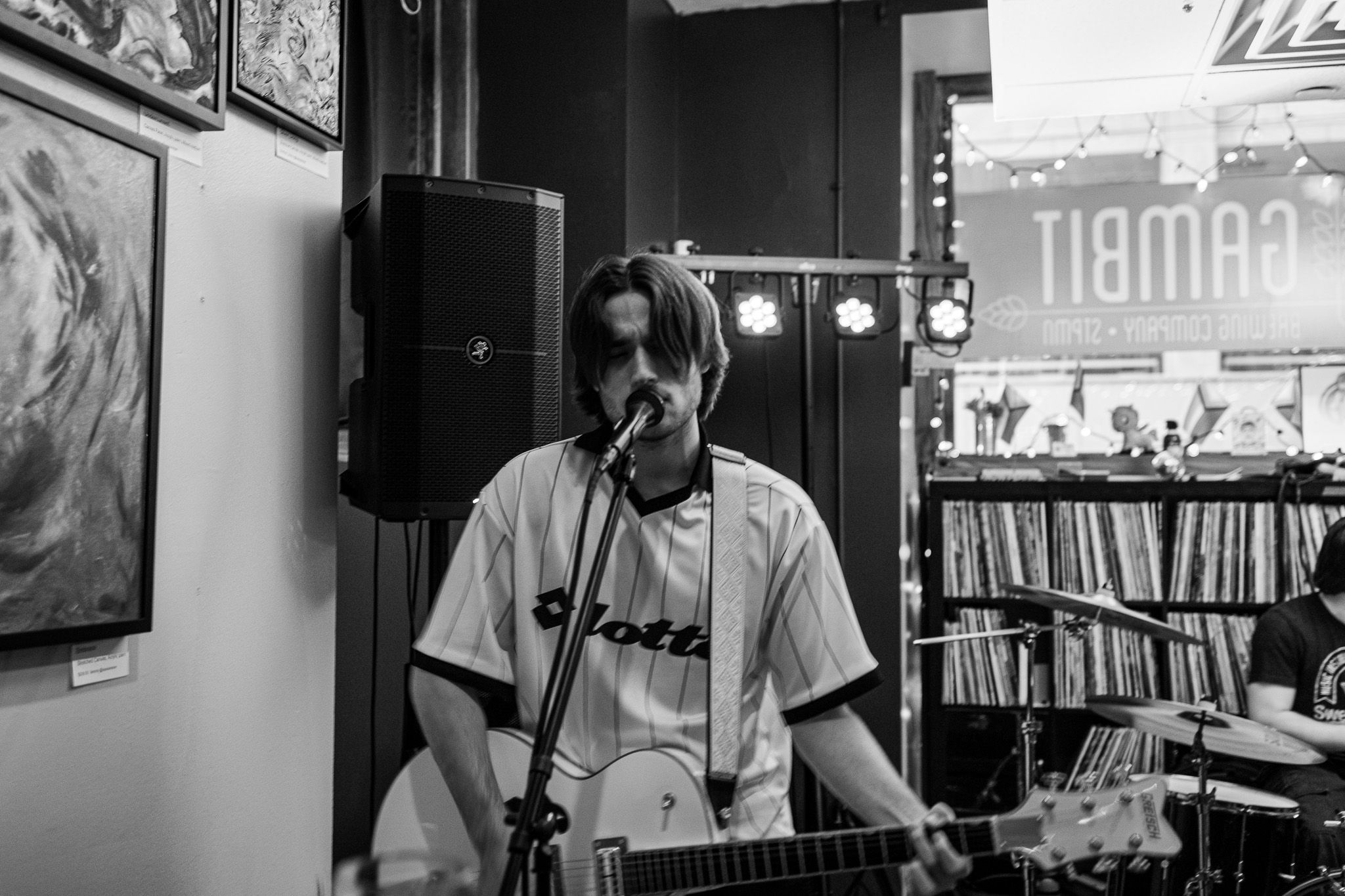 Black and white photo of a musician singing and playing guitar at an indoor record store live performance.