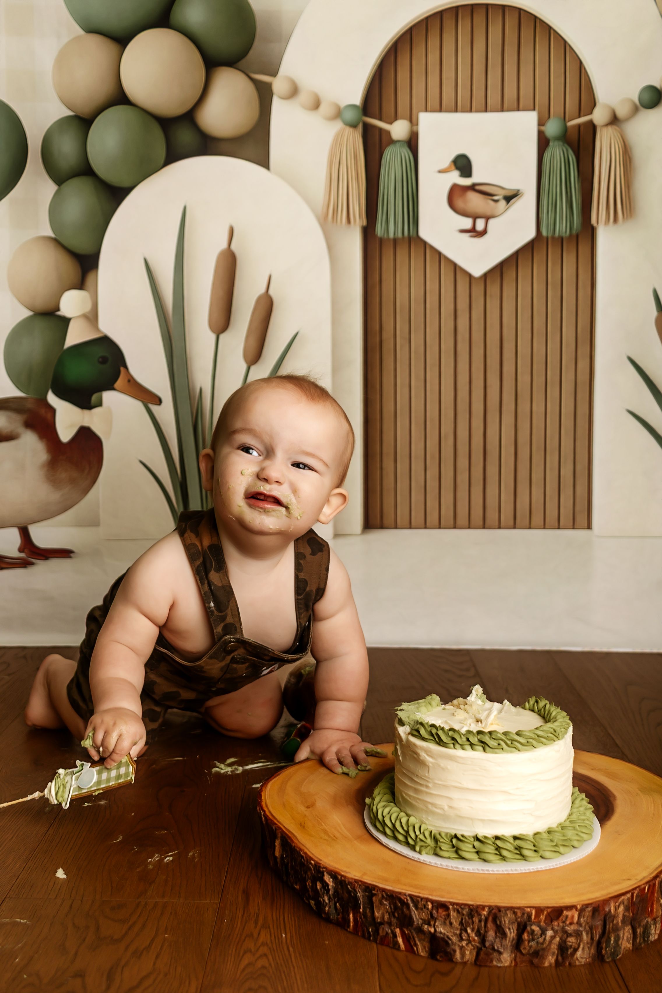 Baby's first birthday cake smash with duck theme, green and cream cake on wood slice, balloon backdrop.