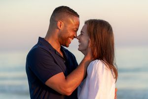 Romantic couple sharing an intimate moment on a beach at sunset, smiling and touching foreheads tenderly.