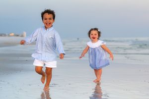 Two happy children running and laughing together on a sunny beach shoreline.