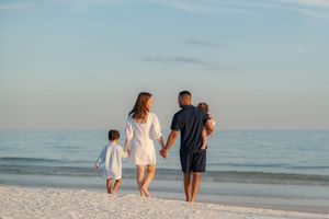 Family of four walking hand-in-hand along a serene white sand beach at sunset.