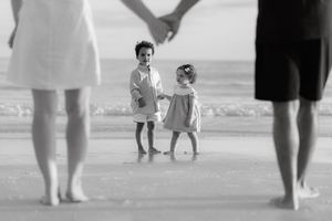Black and white photo of two young children holding hands on a beach while their parents hold hands around them.