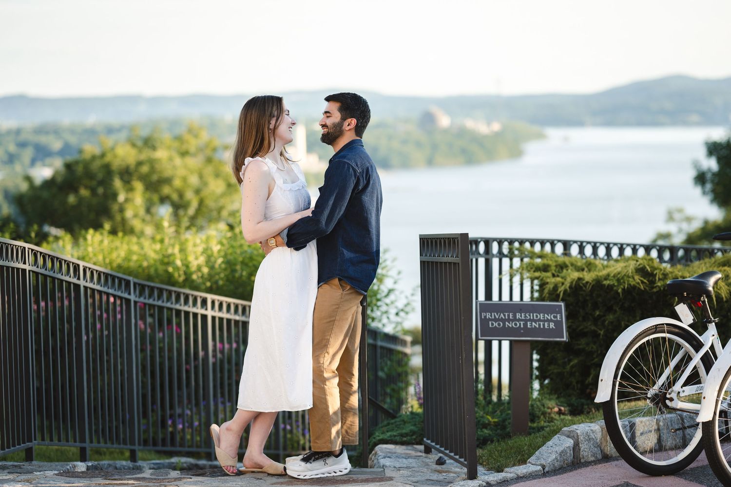 Engaged couple embrace and laugh at The Abbey Inn and Spa in Peekskill, NY in front of expansive Hudson River view on top of bluff.