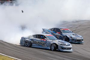 Two drift cars surrounded by smoke compete on a race track during a motorsport event.
