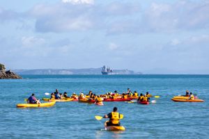 Group of kayakers in yellow kayaks on calm blue ocean waters with a large ship in the distance.