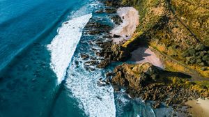 Aerial view of dramatic rocky coastal cliffs with crashing white ocean waves.