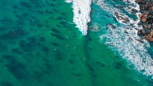 Aerial view of surfers in turquoise ocean water near rocky coastline.