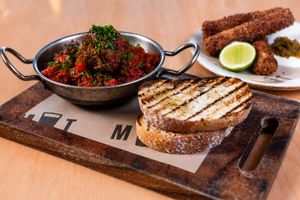 Rustic serving board with spicy meatballs in tomato sauce, grilled sourdough bread, and crispy sides.