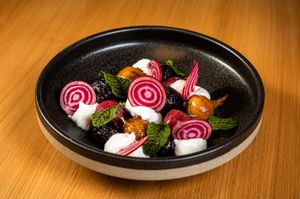 Elegant beet salad with mozzarella, fresh mint, and colorful vegetables served in a black ceramic bowl.