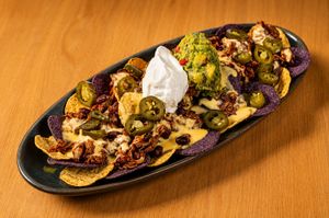 Loaded nachos with jalapeños, guacamole, sour cream, cheese sauce, and pulled meat on blue corn chips.