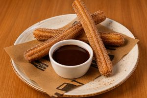 Golden churros with cinnamon sugar served with a rich chocolate dipping sauce on a ceramic plate.