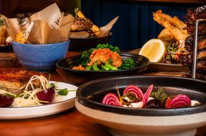 Spread of restaurant dishes including beet salad, crispy proteins, and greens on a wooden table.