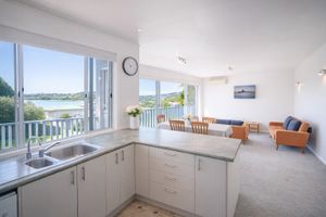 Bright open-plan kitchen with white cabinetry, river views, and a spacious living area beyond.