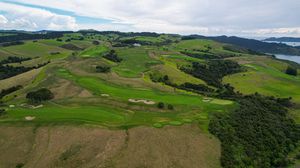 Aerial view of a lush green golf course with rolling hills and ocean views.