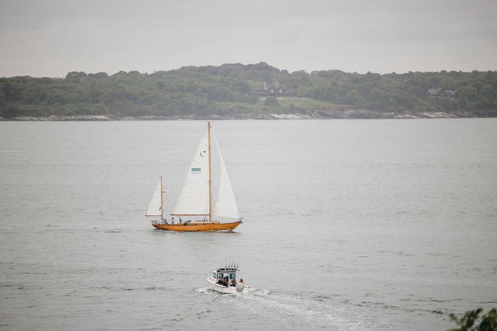 A classic wooden sailboat and a small motorboat Waterfront wedding ceremony at OceanCliff Hotel in Newport, Rhode Island. Wedding photograph